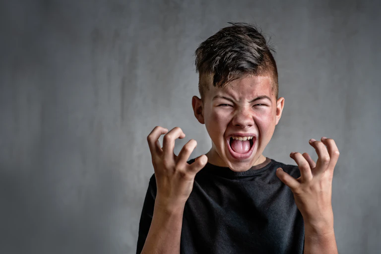 Teen boy screaming in anger on dark background.