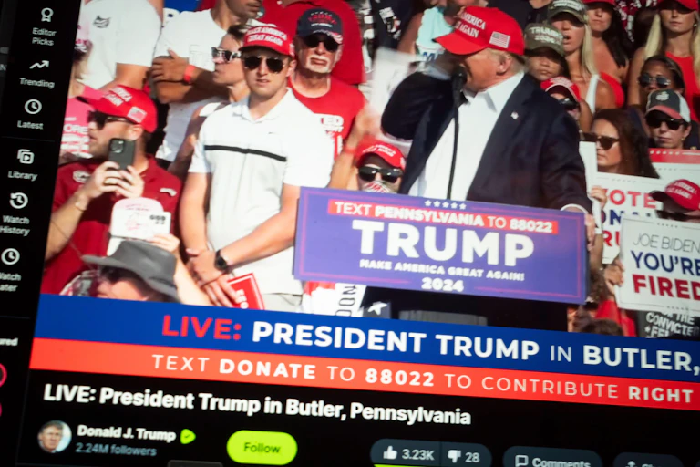 Screenshot of Donald Trump holding his ear after being hit by a bullet.