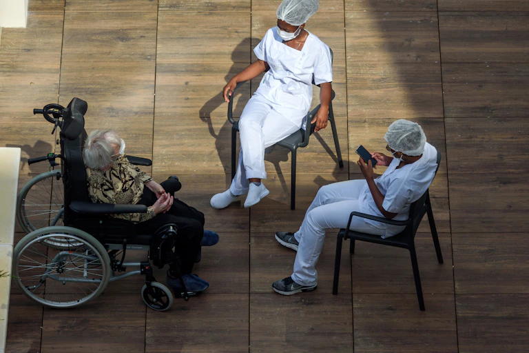 Une personne âgée dans un fauteuil roulant et deux personnes appartenant apparamment au monde médial