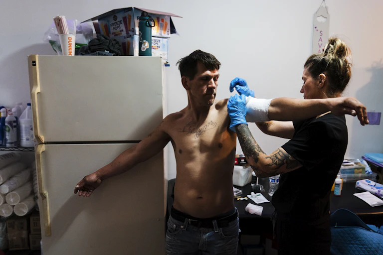 Nurse wearing surgical gloves bandages upper arm of shirtless man