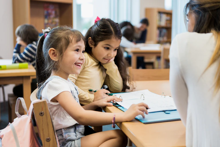 Two young girls sit at a school desk.