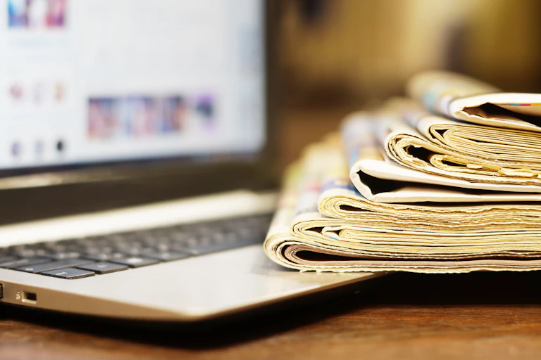 A stack of newspapers beside a laptop
