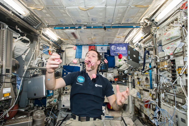 Photo of a man on the International Space Station pretending to eat one of several macarons floating in the air in front of him.