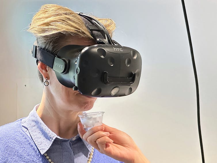 Photo of a person wearing a VR headset and sniffing a small container held under their nose.