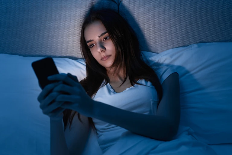 Young woman staring at phone in bed