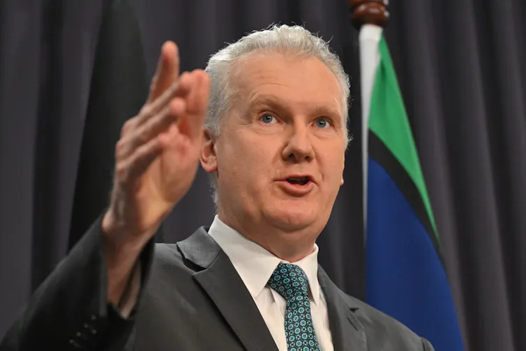 A man in a suit and tie gesticulates as he speaks
