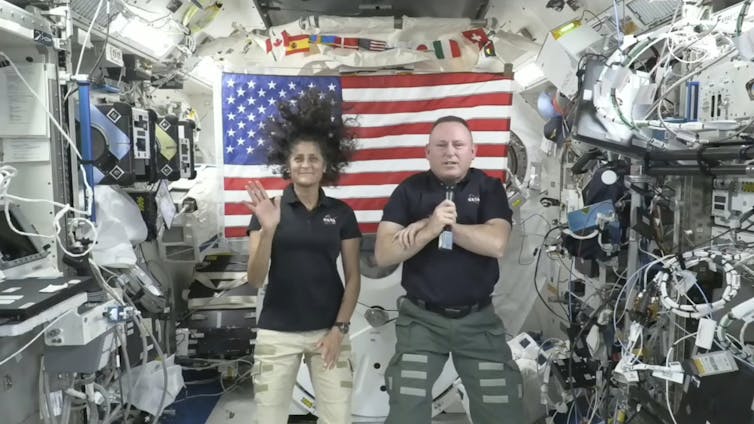 A man and a woman float on a spaceship in front of the US flag.