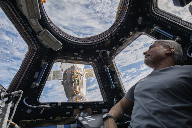 A man looking through the window of the International Space Station.