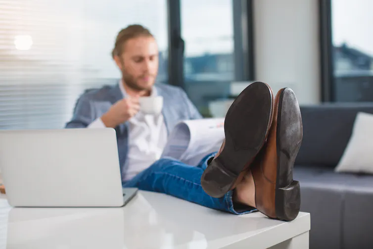 A man drinking coffee with his feet on the desk.