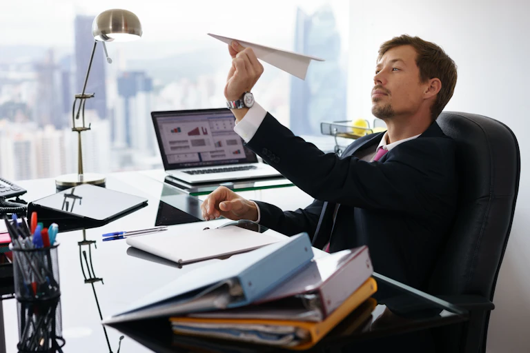 A man throwing a paper plane at his desk.