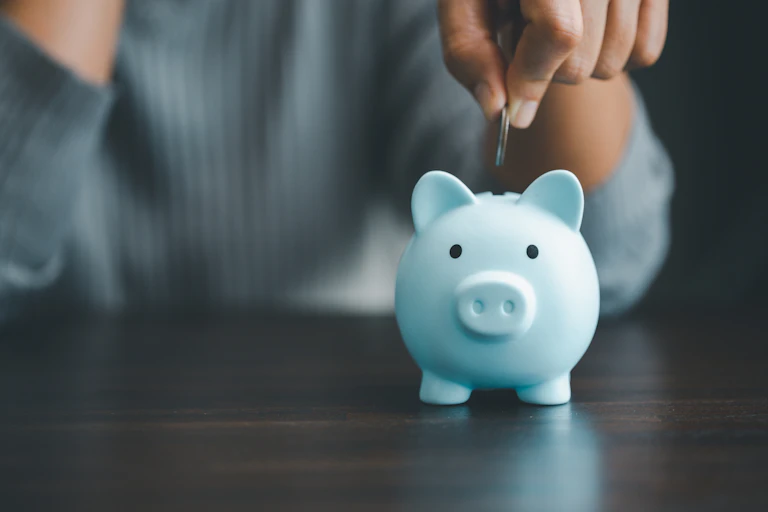 A hand dropping a coin into a piggy bank