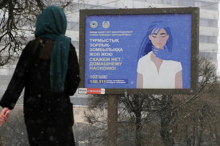 Une femme passe devant une affiche comportant des numéros de téléphone d'assistance aux victimes de violence domestique et indiquant « Dites non à la violence domestique ! »