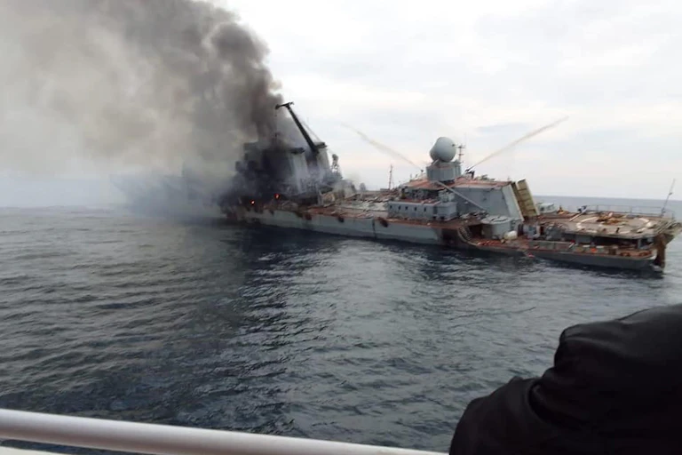 A warship slumps to one side as smoke pours from its superstructure.