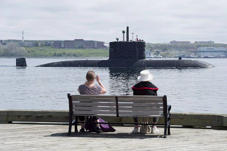 Two people sit on a bench watching a partially submerged submarine go by.