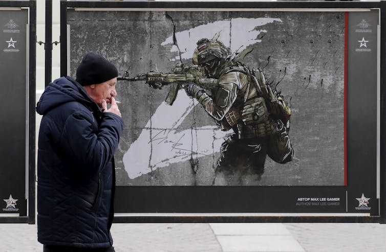 A man smoking a cigarette walks past an artwork depicting a Russian soldier with a large z in the background.