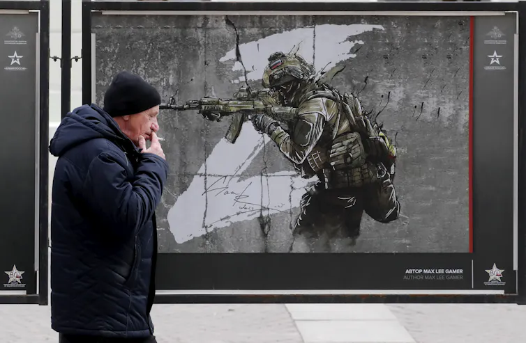 A man smoking a cigarette walks past an artwork depicting a Russian soldier with a large z in the background.
