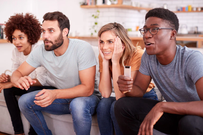 Four people sitting on sofa watching TV.