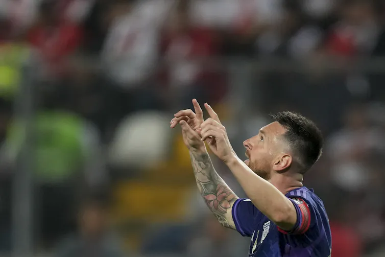 Man in a soccer uniform, seen from the chest up, pointing toward the sky with his index fingers