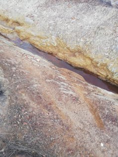 A rivulet of brown water running through rocks out in the open