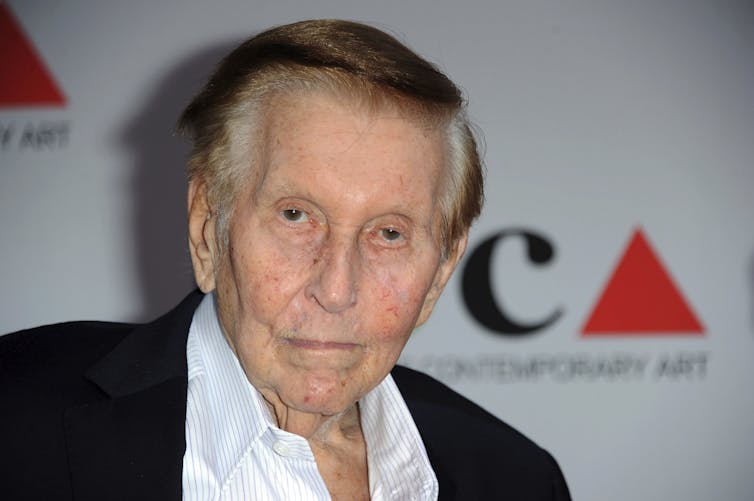 Older man in a blazer and collared shirt without a tie.