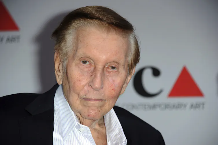 Older man in a blazer and collared shirt without a tie.