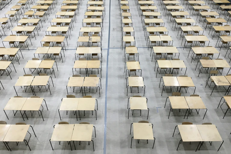 Rows of tables and chairs set up in a hall for an exam.