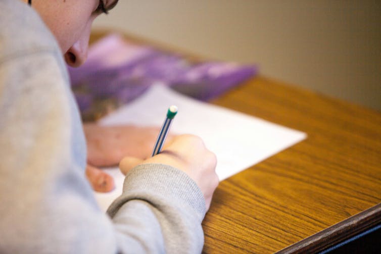 A young person holds a pencil and writes on a sheet of paper.