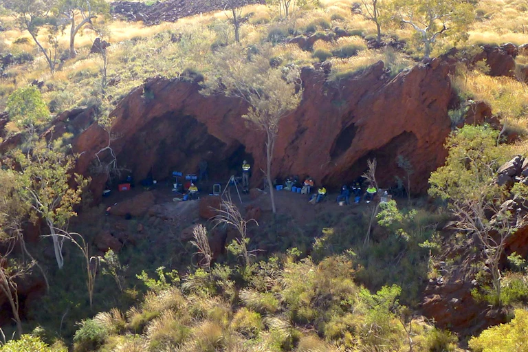 Aerial photo of a group of people at the foot of a cliff contains caves.