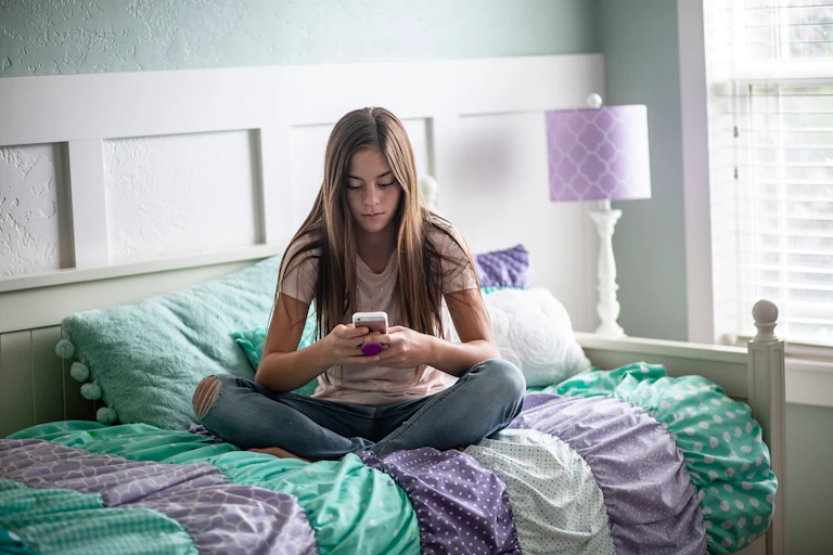 A teenage girl sitting on her bed on her phone.