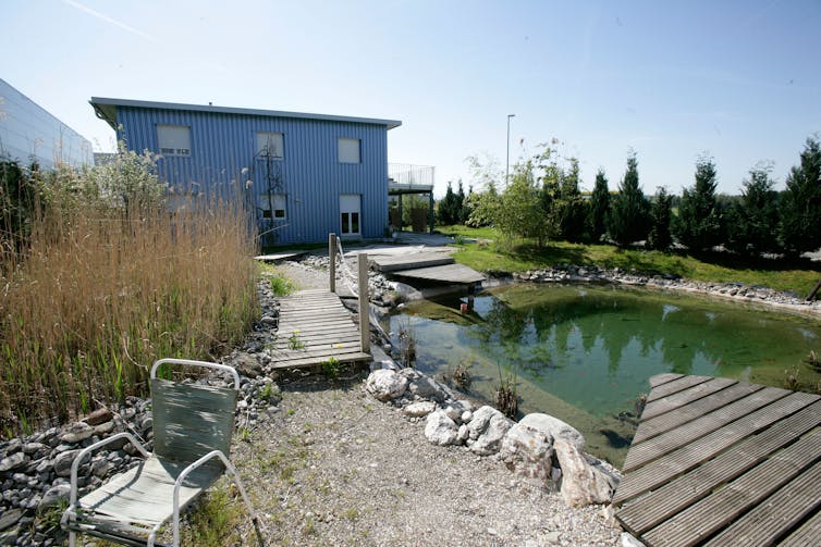 Blue prefab building with a small lake in front of it.