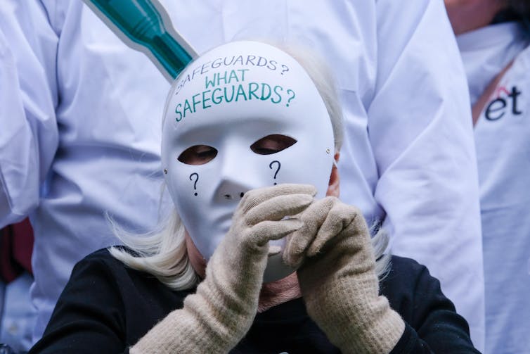 Anti-assisted dying protester wearing a white mask with the words 'what safeguards?'
