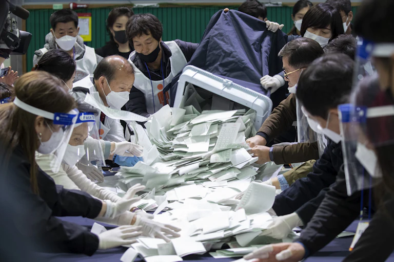 Men and women in masks sift through white sheets of paper.