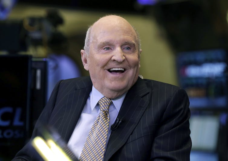 An older man in a suit and tie, smiling.