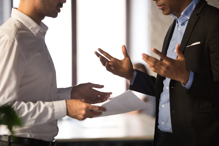 Close up of two men, seen from the chin down, gesturing and speaking to one another in what appears to be a heated discussion