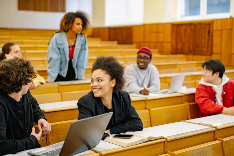 Six young people sit in a lecture theatre. They are laughing and talking to one another.