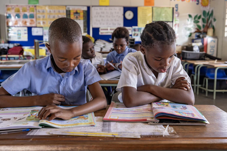 Two school children sitting together at a desk reading from books in front of them