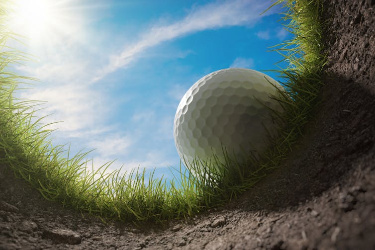 Golf ball just on the tipping point of the hole.