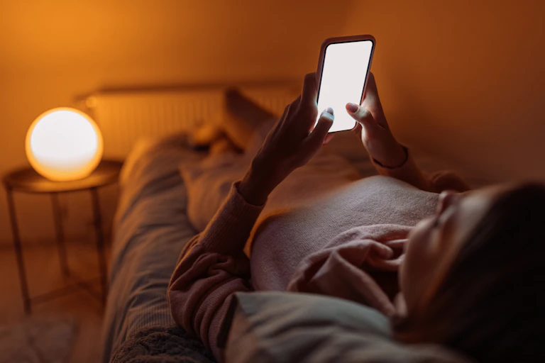 Young woman lying in bed looking at her phone.