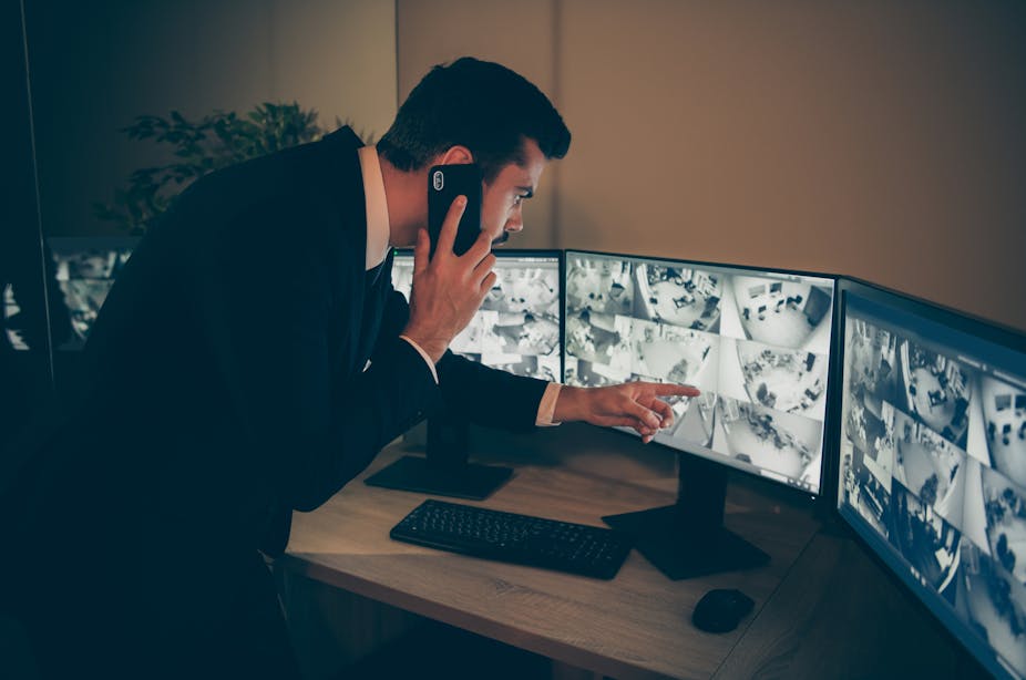 A man points at a CCTV screen while talking on a cellphone.