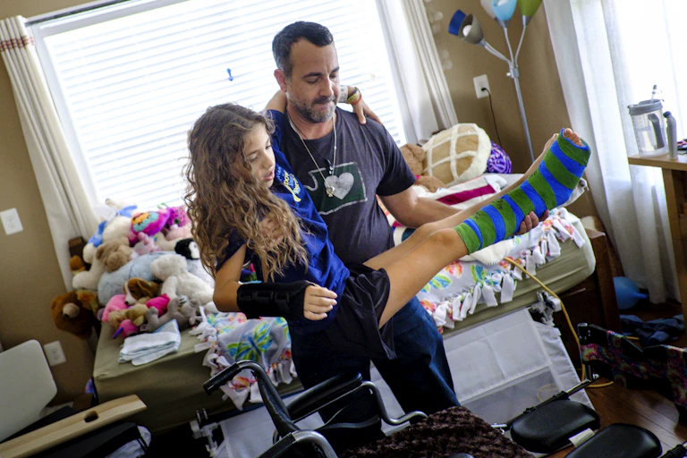 Man lifts tween girl before placing her in a wheelchair.
