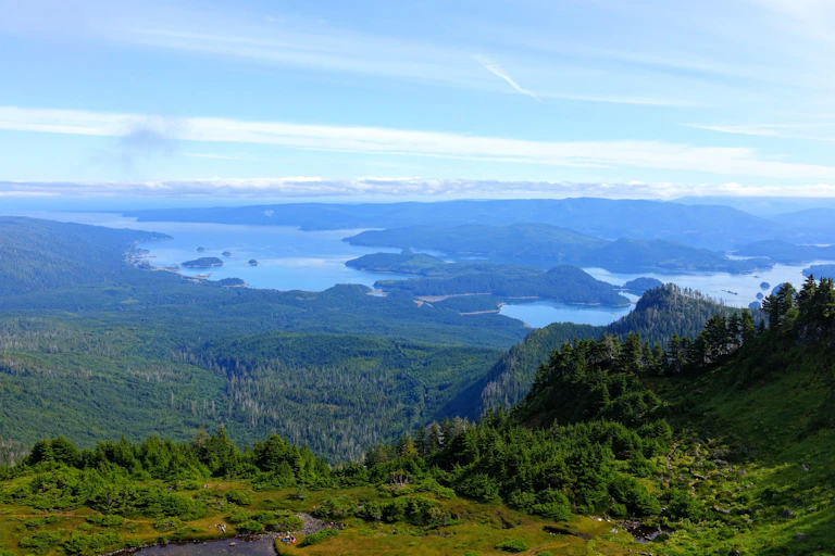 A scenic view of a green landscape from a mountain summit with a sea shore in the distance.
