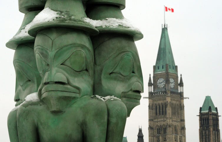 A green sculpture featuring three men. The clock tower of the Canadian parliament can be seen in the background.