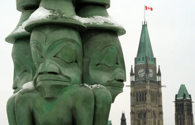 A green sculpture featuring three men. The clock tower of the Canadian parliament can be seen in the background.
