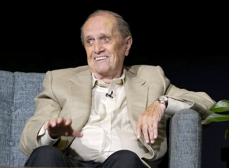an elderly white man appears to laugh sitting on a couch