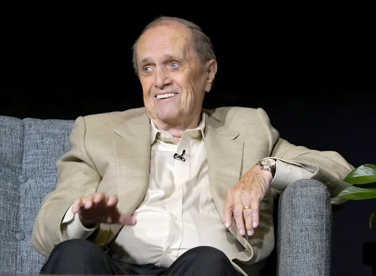 an elderly white man appears to laugh sitting on a couch