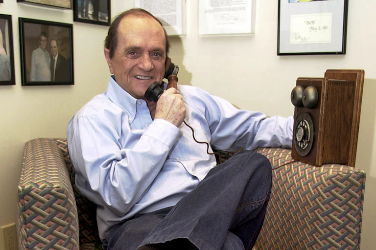 a sitting white man holds an old telephone receiver to his ear