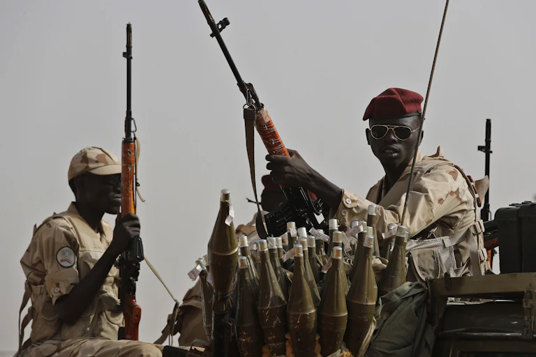 A man in army fatigues and a red beret is surrounded by ammunition.