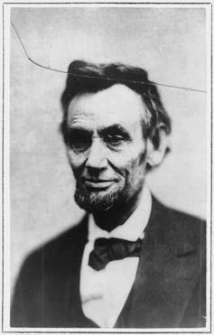 A black and white portrait of a bearded man in a suit and bow tie, taken from the chest up.