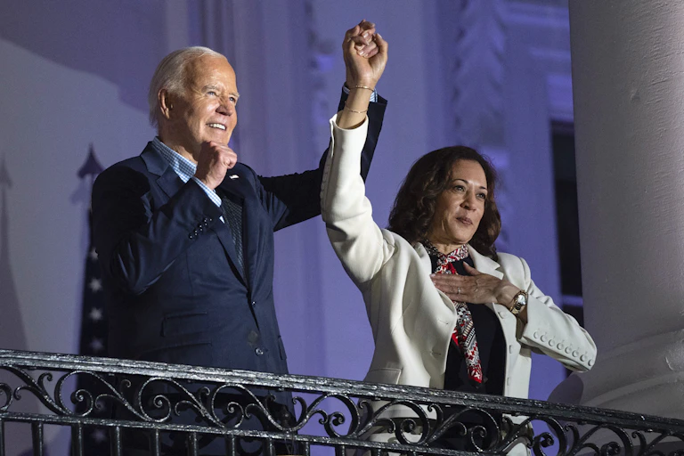 A white man in a suit and a Black woman hold hands in the air