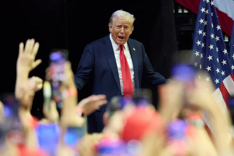 A man in a suit and red tie enthusiastically addresses a crowd at a rally